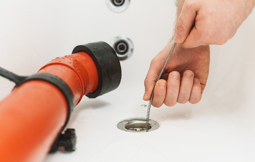 Plumber using drain snake to unclog bathtub Plumber using drain snake to unclog bathtub
