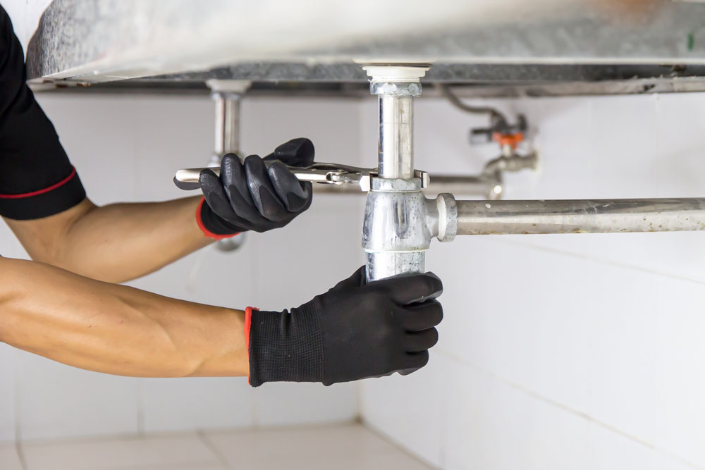 plumber using a wrench to repair a water pipe under the sink Gilbert, AZ plumber using a wrench to repair a water pipe under the sink Gilbert, AZ