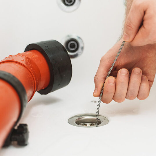 Plumber using drain snake to unclog bathtub